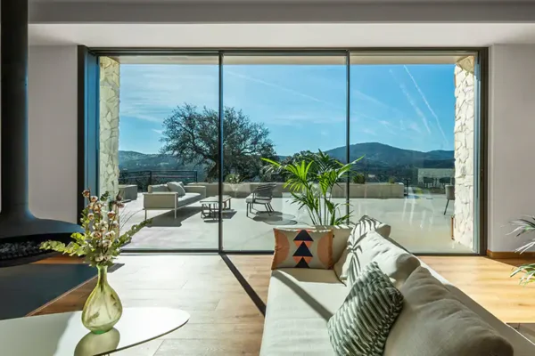 Sofa placed directly beside a floor-to-ceiling aluminium sliding door, with sunlight falling across the floor where occupants sit near the glass
